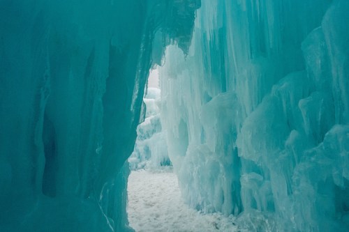 A narrow icy passageway with towering blue ice formations on either side, leading to a bright light in the distance.