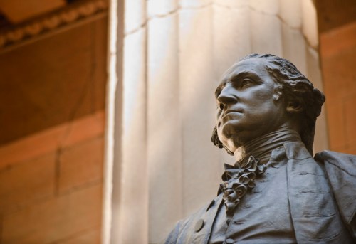 A close-up of a statue of a historical figure, set against a column in a well-lit interior space.