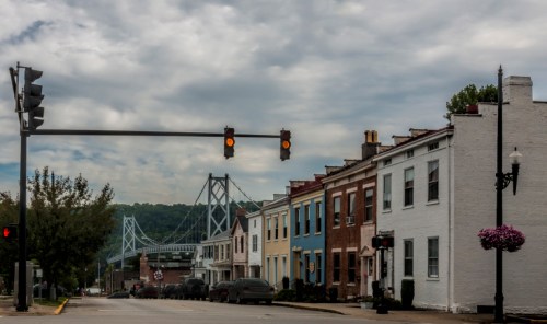A street view featuring colorful houses, traffic lights, and a bridge in the background under a cloudy sky.