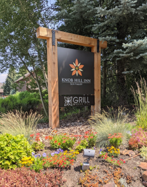 Sign for Knob Hill Inn in Sun Valley, featuring a flower logo and Grill restaurant, surrounded by colorful flowers and greenery.