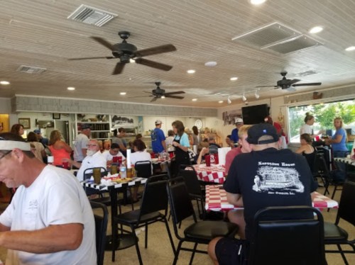 A busy restaurant interior with patrons at tables, fans overhead, and a lively atmosphere.