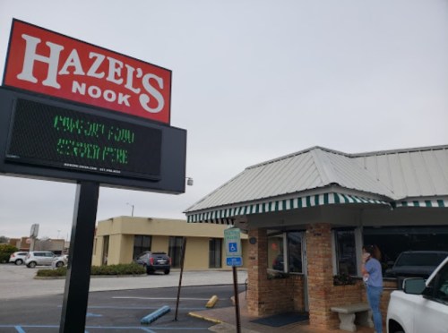 Sign for Hazel's Nook outside a restaurant with a person standing nearby, cloudy sky in the background.