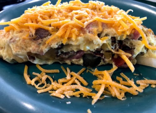 A cheesy omelette filled with vegetables, topped with shredded cheddar cheese, served on a green plate.
