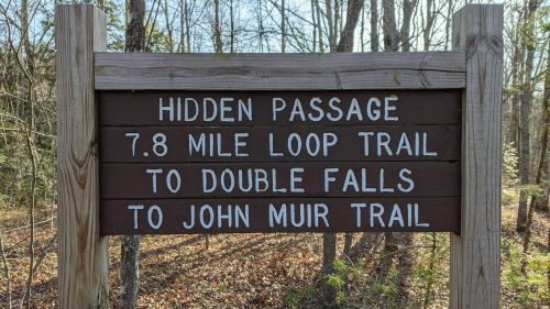 Wooden sign indicating the Hidden Passage 7.8 mile loop trail to Double Falls and John Muir Trail in a forested area.