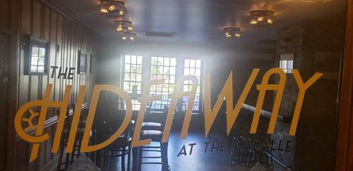 A view through a glass door featuring the sign "The Hideaway at The LaSalle" with a bright, inviting interior behind it.