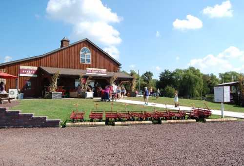 A rustic bakery with a wooden exterior, surrounded by people and red wagons on a sunny day.