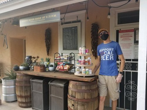 A man in a blue shirt and mask stands by a rustic bar with snacks and drinks, promoting happy hour.