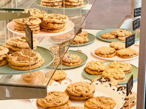 A display of various cookies on plates, including chocolate chip and oatmeal raisin, with labels on stands.