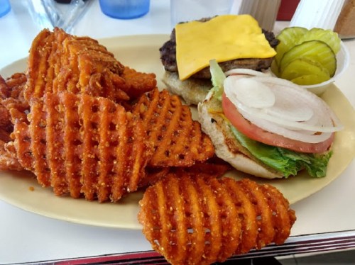 A plate of waffle fries and a cheeseburger with lettuce, tomato, and pickles on a bun.