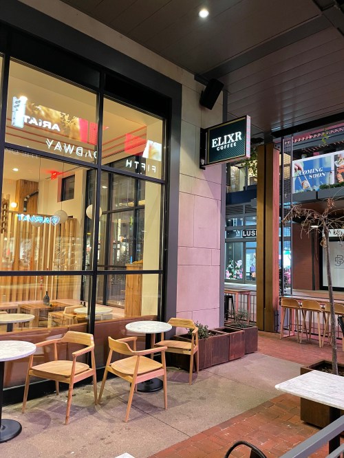 Exterior view of Elixr Coffee shop with outdoor seating and large windows, showcasing a modern urban atmosphere.