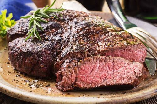 A perfectly cooked steak on a plate, garnished with rosemary and sprinkled with salt and pepper.