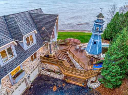 Aerial view of a lakeside home with a wooden deck and a blue lighthouse structure nearby.