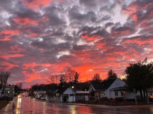Vibrant sunset with red and orange clouds over a quiet street lined with shops, reflecting on wet pavement.