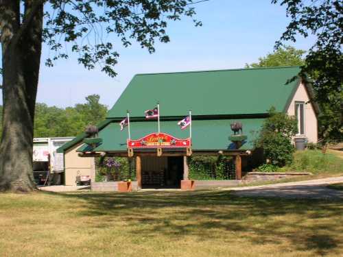 A building with a green roof, flags flying, surrounded by trees and grass on a sunny day.