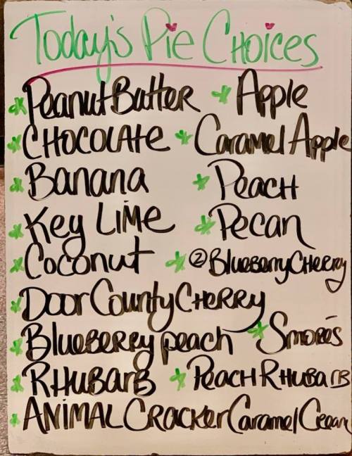 A whiteboard listing today's pie choices, including flavors like peanut butter, chocolate, and key lime.