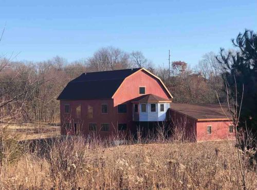 A red barn-style house surrounded by dry grass and trees under a clear blue sky.