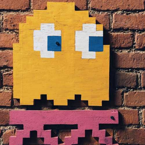 Colorful pixel art of a ghost character on a brick wall, featuring yellow and blue elements with a pink base.