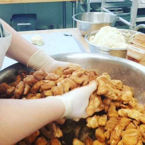 A person’s hands mixing a large bowl of golden-brown fried food in a kitchen setting.