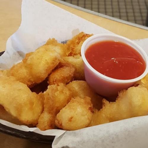 A plate of golden, crispy fried snacks served with a small cup of red dipping sauce.