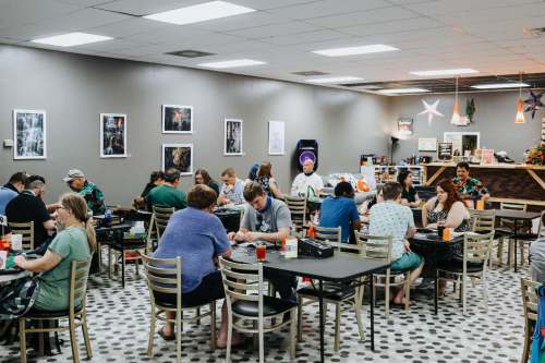A lively game café with people seated at tables, playing games and enjoying drinks in a cozy, well-lit space.