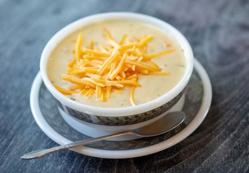 A bowl of creamy soup topped with shredded cheese, served on a saucer with a spoon beside it.