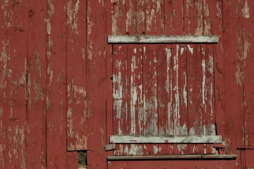 Close-up of a weathered red barn wall with peeling paint and a wooden shutter.