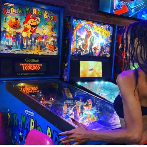 A person plays a vintage Super Mario Bros. pinball machine in a colorful arcade setting.