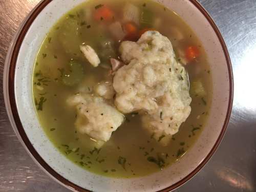 A bowl of soup with vegetables and two large dumplings, garnished with herbs.