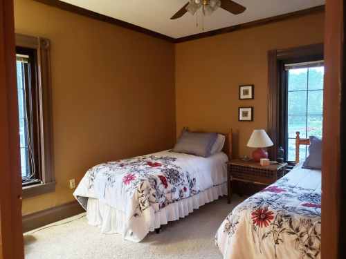 Cozy bedroom with two twin beds, floral bedding, a lamp, and windows letting in natural light.