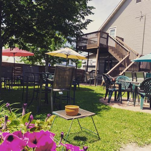 Outdoor seating area with tables, umbrellas, and flowers, set against a sunny backdrop of a building and trees.