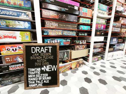 A cozy game store with shelves stacked high with board games and a chalkboard listing events and new items.