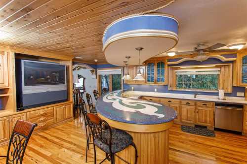 A spacious kitchen with wooden cabinets, a curved bar, and a large TV, featuring blue accents and a cozy atmosphere.