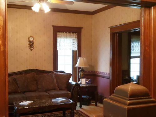 Cozy living room with a brown sofa, lamp, and decorative wallpaper, featuring a clock and a view into another room.