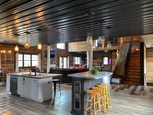 Modern open-concept kitchen and living area with wooden accents, bar stools, and a staircase in a cozy, rustic setting.