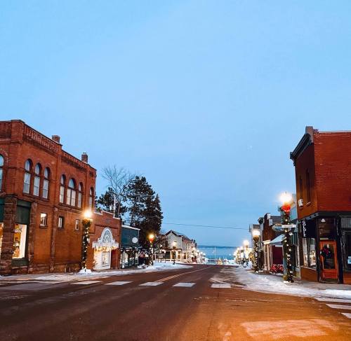 A quiet winter street scene with historic buildings, snow-covered ground, and soft evening light.