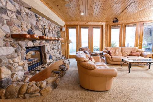 Cozy living room with a stone fireplace, leather furniture, and large windows overlooking a scenic view.