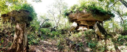 A panoramic view of large, flat-topped rock formations surrounded by lush greenery and trees.