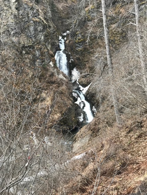 A cascading waterfall flows down a rocky slope, surrounded by bare trees and rugged terrain.