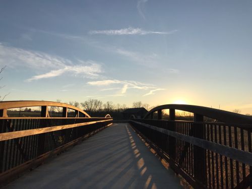 A wooden bridge at sunset, with a clear sky and shadows stretching across the path.