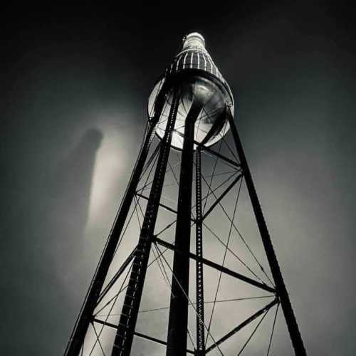 A tall, industrial tower rises against a dark, moody sky, illuminated from within, creating a dramatic silhouette.