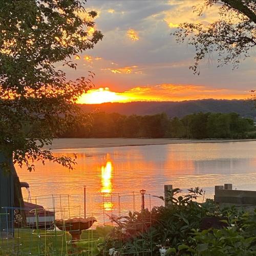 A serene sunset over a lake, with vibrant orange and yellow hues reflecting on the water and lush greenery in the foreground.