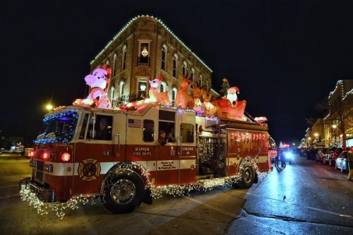 A festive fire truck adorned with lights and holiday decorations, featuring large inflatable reindeer and Santa figures.