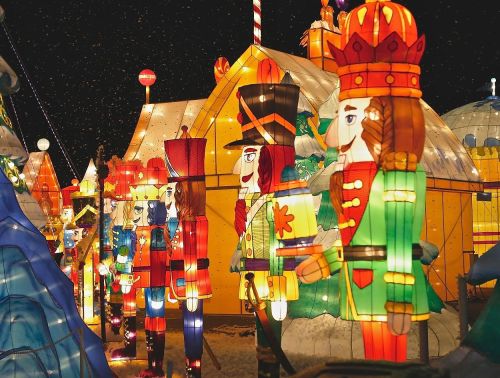 Colorful illuminated nutcracker figures stand in front of festive tents, creating a magical winter scene at night.