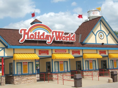 Colorful entrance of Holiday World amusement park with yellow awnings and a rainbow sign against a blue sky.