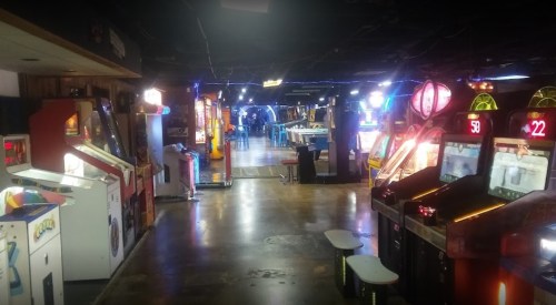 A dimly lit arcade with various vintage game machines and neon lights lining the walls.
