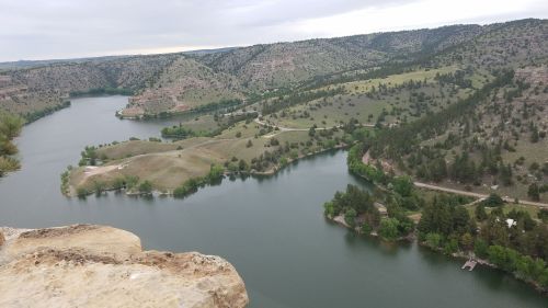 A scenic view of a winding river surrounded by green hills and trees under a cloudy sky.