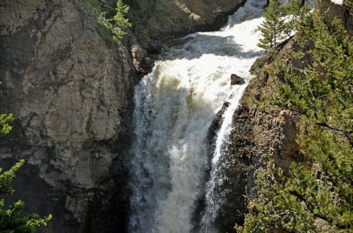 A powerful waterfall cascading down rocky cliffs, surrounded by lush greenery and rugged terrain.
