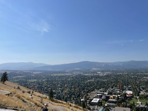A panoramic view of a valley and mountains under a clear blue sky, with a cityscape in the foreground.