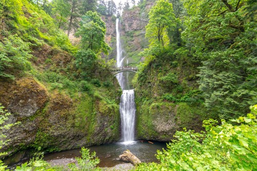 A scenic view of a waterfall cascading between lush green cliffs, with a bridge spanning above the falls.