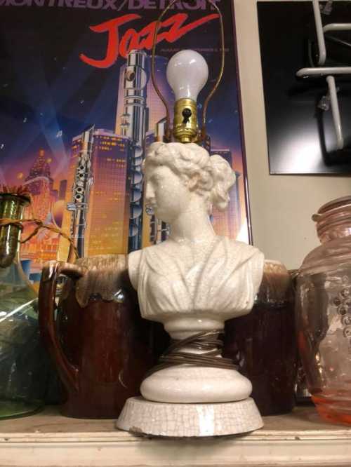 A decorative lamp featuring a bust of a woman, set against a backdrop of vintage items and a jazz poster.